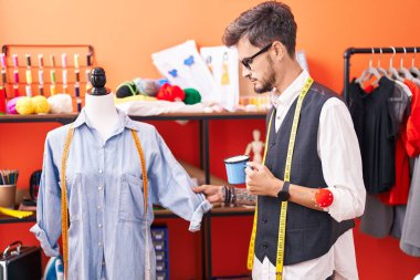 Genç İspanyol terzi atölyede manikinin yanında kahve içiyor.