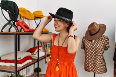 Orta yaşlı İspanyol kadın perakende dükkanında siyah şapkaya bakıp gülümsüyor.