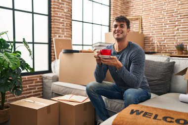 Genç İspanyol adam yeni evindeki kanepede kahve içiyor.