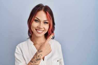 İzole edilmiş arka plan üzerinde günlük beyaz gömlek giyen genç beyaz kadın mutlu ve doğal bir ifadeyle el ve parmak ile yüzünü gösteren bir gülümseme ile 