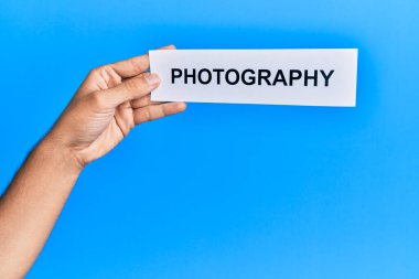 Hand of caucasian man holding paper with photography word over isolated blue background