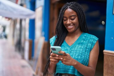 Afro-Amerikalı kadın sokakta akıllı telefon kullanarak kendine güveniyor.