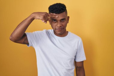 Sarı arka planda duran genç İspanyol adam alnındaki sivilceden mutsuz olduğunu gösteriyor, siyah başlıktaki çirkin enfeksiyon. sivilce ve deri problemi 