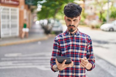 Young hispanic man using touchpad standing at street