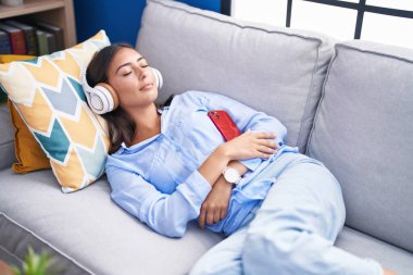 Genç, güzel İspanyol kadın evdeki kanepede müzik dinliyor.