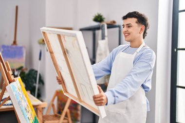 Young non binary man artist smiling confident holding draw canvas at art studio