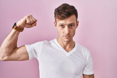 Caucasian man standing over pink background strong person showing arm muscle, confident and proud of power 