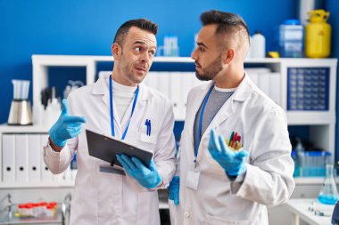Two men scientists reading document with relaxed expression at laboratory