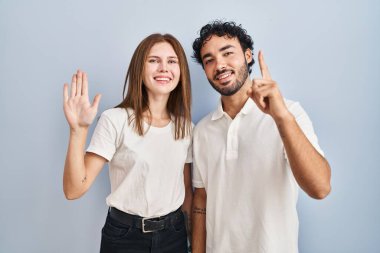 Genç çift gündelik giysiler giyip 6 numaralı parmaklarını göstererek gülümseyerek mutlu ve kendinden emin bir şekilde ayakta duruyorlar.. 