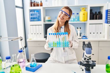 Laboratuvarda test tüpleri tutan bilim adamı üniforması giyen genç sarışın kadın.