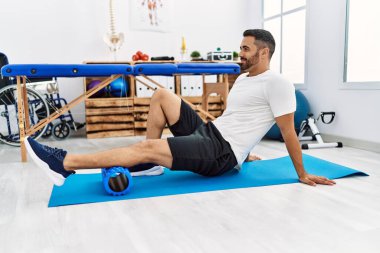 Genç İspanyol hasta gülümsüyor. Bacak rehabilitasyonu seansı için klinikte köpük rulo kullanıyor.