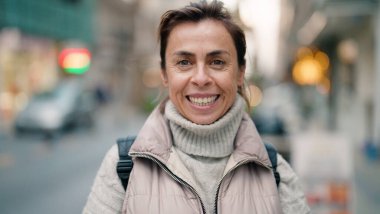 Orta yaşlı İspanyol kadın sokakta kendine güvenerek gülümsüyor.