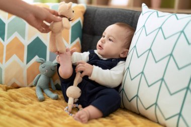 Sevimli çocuk evde kanepede oyuncak ayıyla oynuyor.