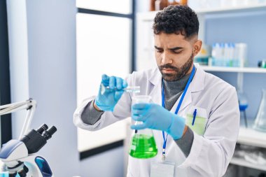 Laboratuvarda sıvı ölçen bilim adamı üniforması giyen İspanyol genç adam.