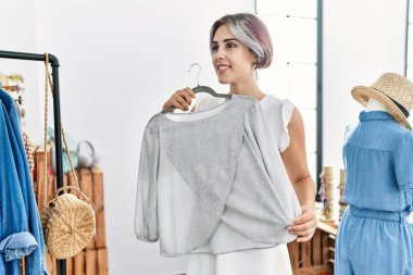 Genç beyaz kadın gülümseyerek giyim mağazasından kıyafet seçiyor..