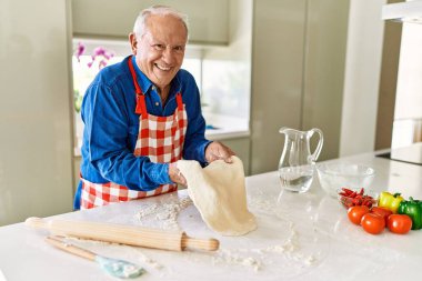 Senior man smiling confident holding dough with hands at kitchen