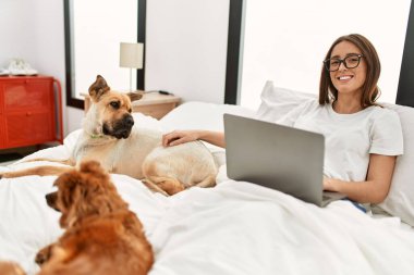 Genç İspanyol kadın, yatak odasında köpeklerle birlikte dizüstü bilgisayar kullanıyor.