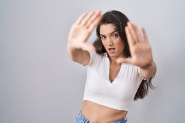 Young teenager girl standing over white background doing frame using hands palms and fingers, camera perspective 