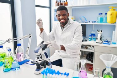 African american man working at scientist laboratory screaming proud, celebrating victory and success very excited with raised arm 
