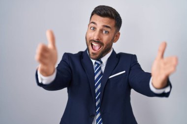 Yakışıklı, takım elbiseli ve kravatlı bir adam kameraya bakıp sarılmak için gülümsüyor. Mutluluğu kucaklayan neşeli bir ifade.. 