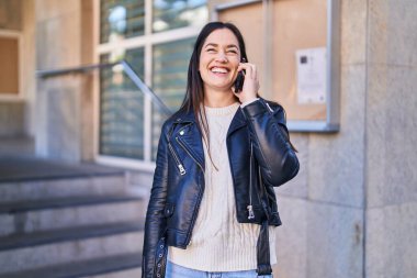 Gülümseyen genç bir kadın caddedeki akıllı telefondan konuşuyor.