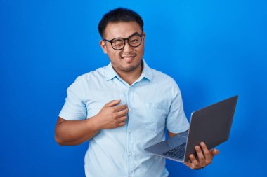 Chinese young man using computer laptop winking looking at the camera with sexy expression, cheerful and happy face. 