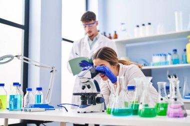 Young man and woman scientists workers using microscope at laboratory clipart