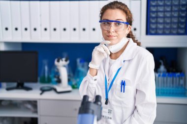 Genç, beyaz bir kadın, laboratuarda çalışan bir bilim adamı. Şüphe üzerine yoğunlaşmıştı. Parmakları çenesinde ve yukarı bakıyordu. 