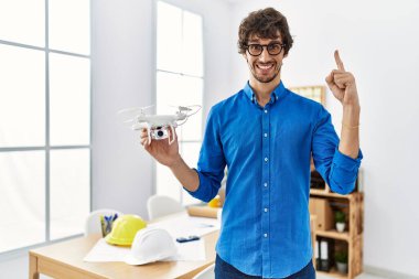 Mimarlık ofisinde İHA kullanan genç İspanyol bir adam bir fikir veya soruyla gülümsüyor ve mutlu bir yüzle işaret ediyor. 