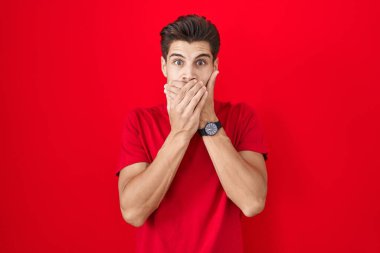 Kırmızı arka planda duran İspanyol genç adam yanlışlıkla ağzını kapatarak şok geçirdi. gizli kavram. 