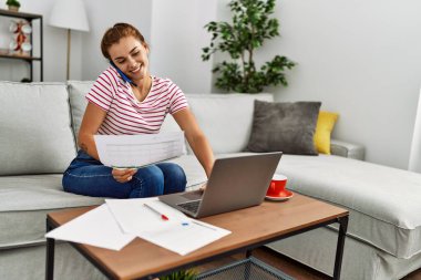 Akıllı telefondan konuşan ve evde çalışan genç bir kadın.