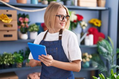 Young blonde woman florist smiling confident using touchpad at florist shop