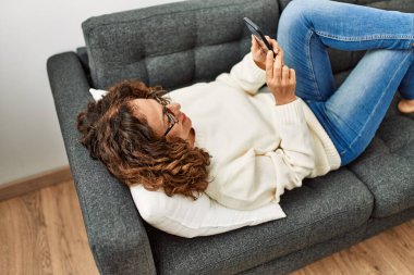 Orta yaşlı İspanyol kadın evde akıllı telefon kullanarak gülümsüyor.