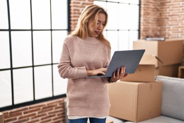 Yeni evinde dizüstü bilgisayar kullanan genç bir kadın.