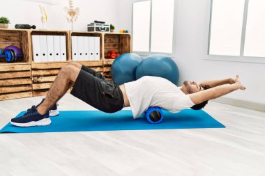 Genç İspanyol adam klinikte köpük silindiri kullanarak rehabilitasyon yapıyor.