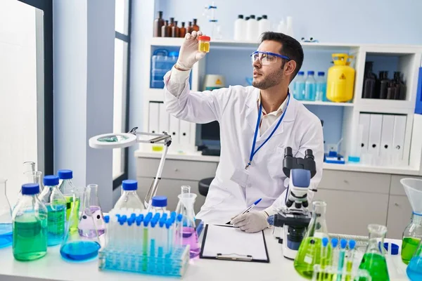 Young Hispanic Man Scientist Looking Urine Test Tube Writing Report — Fotografia de Stock