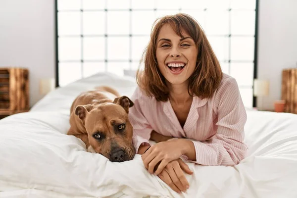 Young caucasian woman smiling confident lying on bed with dog at bedroom