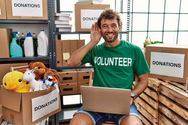 噂やゴシップに耳を傾ける耳の上に手で笑みを浮かべてノートパソコンを使用してボランティアTシャツを着て若いハンサムな男 聴覚障害の概念 — ストック写真