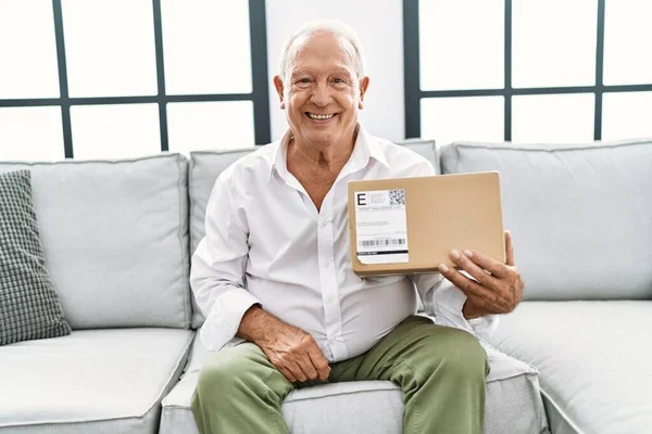 Starší Muž Držící Balíček Doma Vypadá Pozitivně Šťastně Stojící Usmívá — Stock fotografie