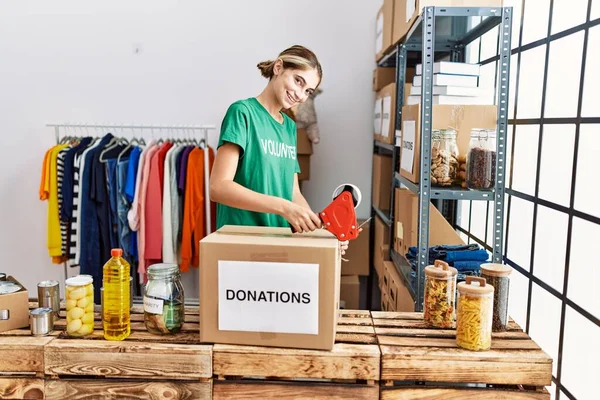 在慈善中心 年轻的高加索妇女身穿志愿者制服 包装捐赠箱 — 图库照片