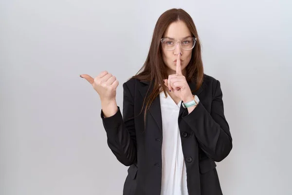 美しいブルネットの女性はビジネスジャケットと眼鏡を身に着けている側に手で指して唇に指で静かになるように求めている 沈黙と秘密の概念 — ストック写真