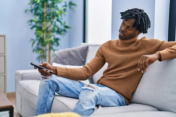 African american man boring watching tv sitting on sofa at home