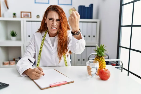 Young Redhead Woman Nutritionist Doctor Clinic Angry Mad Raising Fist — Stock Photo, Image