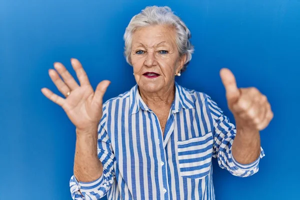 Senior woman with grey hair standing over blue background showing and pointing up with fingers number six while smiling confident and happy.