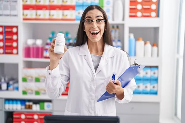 Молодая Брюнетка Работающая Аптеке Держит Таблетки Празднуя Сумасшествие Удивляясь Успеху — стоковое фото