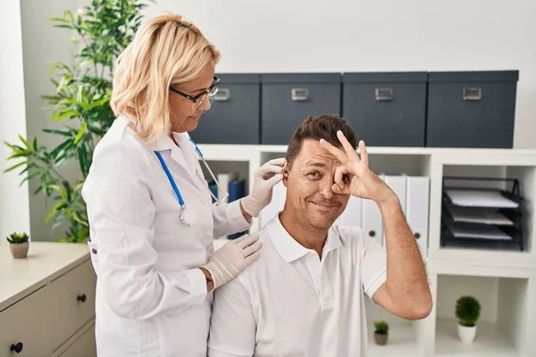 Hispanic man getting medical hearing aid at the doctor smiling happy doing ok sign with hand on eye looking through fingers