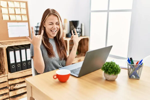 年轻的黑发女人在办公室里用笔记本电脑大喊着 用疯狂的表情举手表决摇滚符号 音乐明星 沉重的概念 — 图库照片