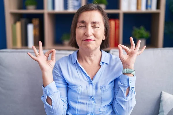 stock image Middle age hispanic woman sitting on the sofa at home relax and smiling with eyes closed doing meditation gesture with fingers. yoga concept. 