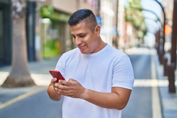 年轻的拉丁男人在街上用智能手机充满自信地微笑 — 图库照片