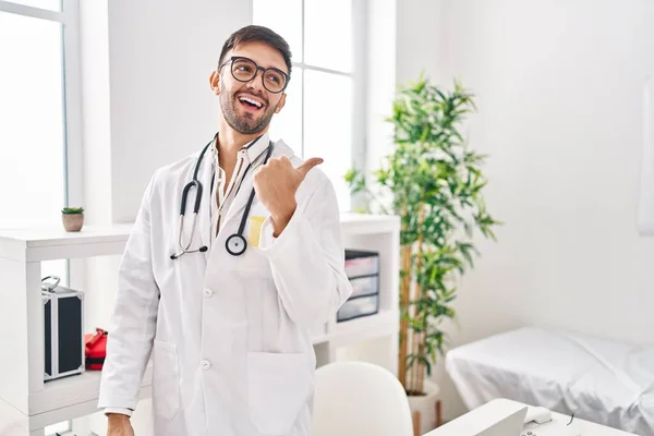 Hispanic Man Wearing Doctor Uniform Stethoscope Pointing Thumb Side Smiling — Stock Photo, Image